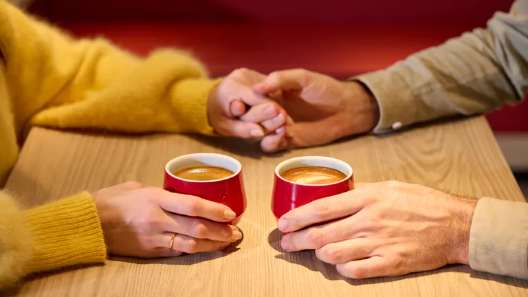 Ein paar hält händchen und sitzt in einem viva kaffee mit zwei kaffeetassen
