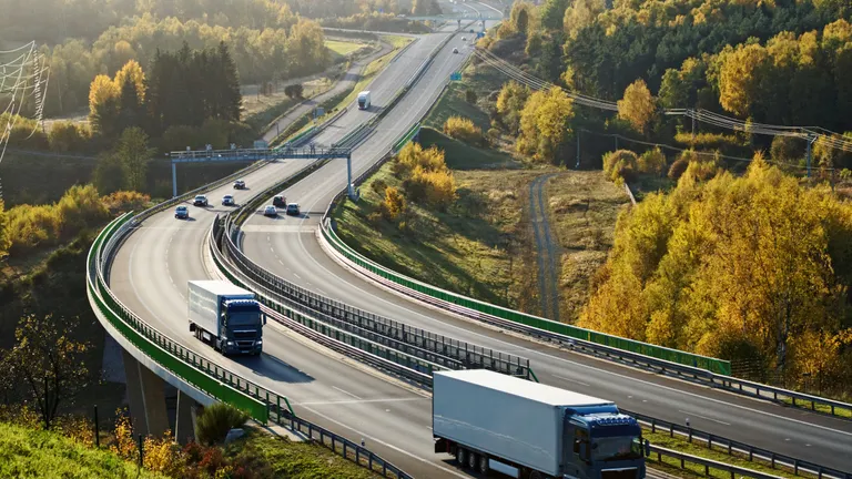 Asphalt highway with electronic toll gates in autumn woodland. Three trucks on the road.