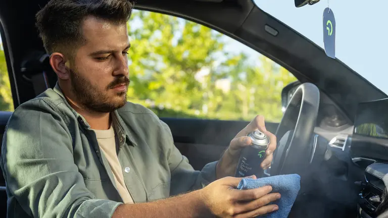 Man sitting in the car, cleaning his interior with a spray