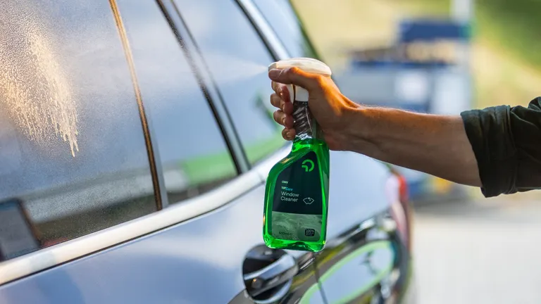 Eine Männerhand sprüht einen grünen TopCare Glasreiniger auf ein Autofenster